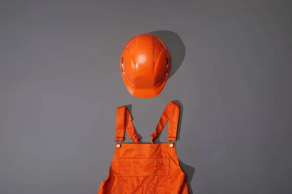 top view of orange helmet and overalls on grey background