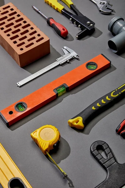 flat lay with brick, measuring tape, spirit level, brick and industrial tools on grey background