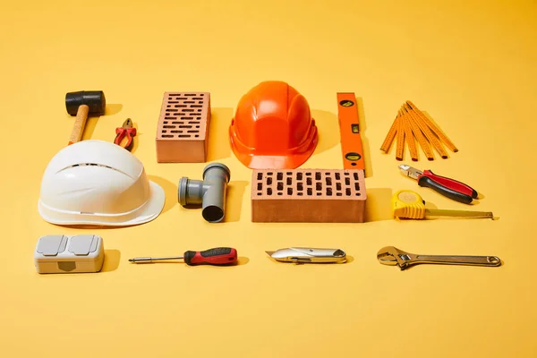 flat lay with bricks, helmets, industrial tools and measuring tape on yellow background