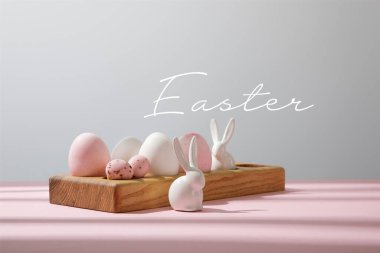 Paskalya yumurtaları ahşap tahtada, dekoratif tavşanlar pembe, gri ve paskalya resimli.