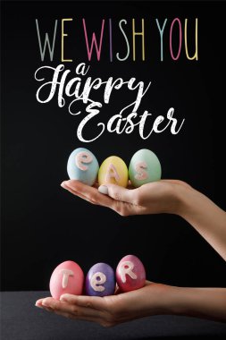 Selective focus of Easter eggs on wooden board on black with we wish you a happy Easter illustration clipart
