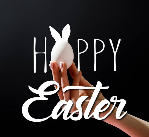Cropped view of woman holding chicken egg isolated on black with happy Easter illustration