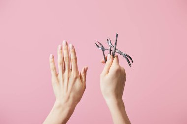 Cropped view of woman holding cuticle pusher and nippers isolated on pink clipart