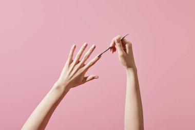 Cropped view of woman doing manicure with cuticle pusher isolated on pink clipart
