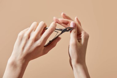 Cropped view of woman doing manicure with cuticle nipper isolated on beige clipart
