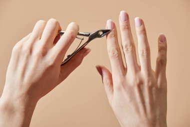 Cropped view of woman cutting cuticle using nipper isolated on beige clipart