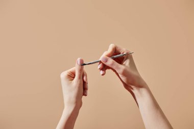 Cropped view of woman doing manicure using cuticle pusher isolated on beige clipart