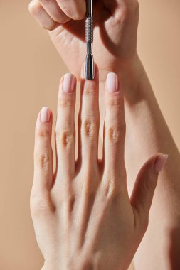 Partial view of woman doing manicure with cuticle pusher isolated on beige clipart