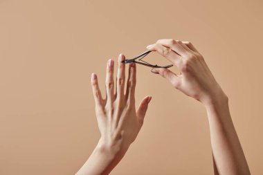 Partial view of woman doing manicure with cuticle nipper isolated on beige clipart