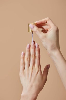 Partial view of woman applying nail polish isolated on beige clipart