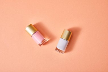 Mercan zemin üzerinde pembe ve beyaz tırnak cilası şişelerinin üst görüntüsü