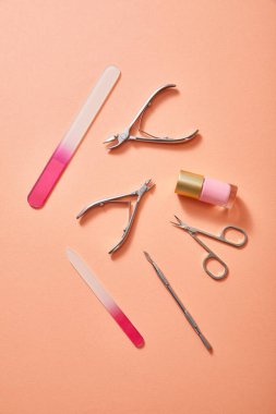 Top view of manicure instruments and bottle of pink nail polish on coral background clipart