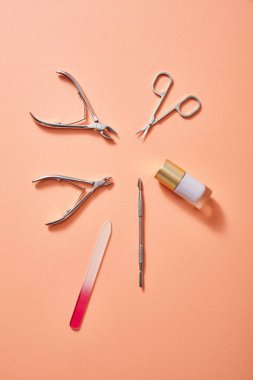 Top view of manicure instruments and bottle of white nail polish on coral background clipart