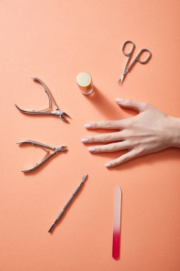 Cropped view of female hand with bottle of nail polish and manicure instruments on coral clipart