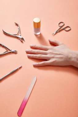 Partial view of female hand with bottle of nail polish and manicure instruments on coral clipart