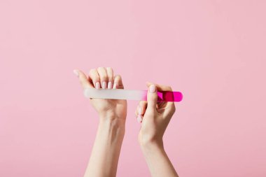 Pembe üzerine izole edilmiş tırnak törpüsü ile manikür yapan kadın görüntüsü.