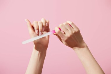 Cropped view of woman filing fingernail with nail file isolated on pink clipart