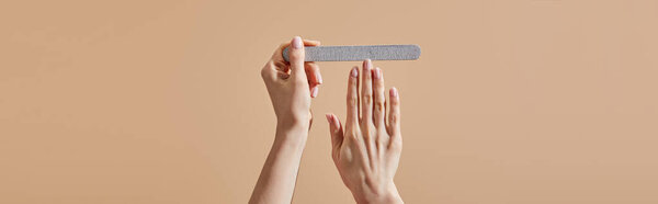 Cropped view of woman filing nail with emery board isolated on beige, panoramic shot