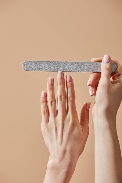 Cropped view of woman filing fingernail with emery board isolated on beige