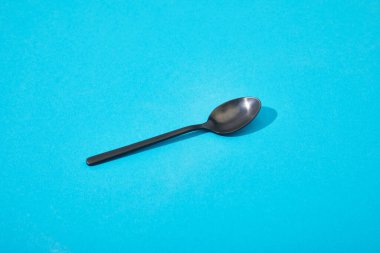 metal shiny black spoon on blue background clipart