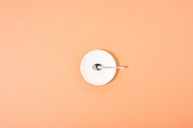 Turuncu zemin üzerinde beyaz yuvarlak plaka üzerinde metal kaşık üst görünümü