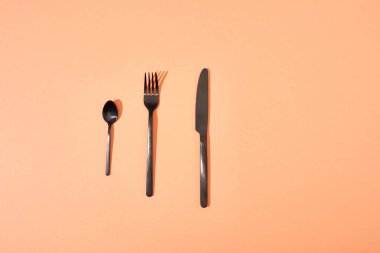 top view of metal shiny black fork, spoon and knife on orange background clipart