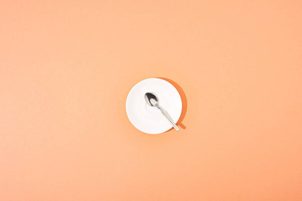 top view of metal spoon on white round plate on orange background