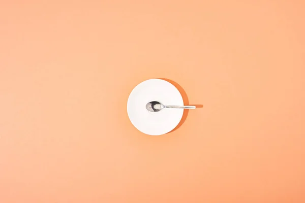 オレンジの背景にある白い丸皿の上からの金属スプーンの眺め — ストック写真