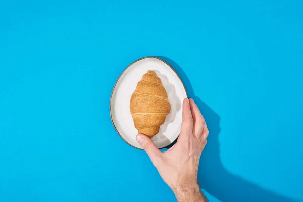 Vista Cortada Homem Segurando Croissant Fresco Placa Fundo Azul — Fotografia de Stock