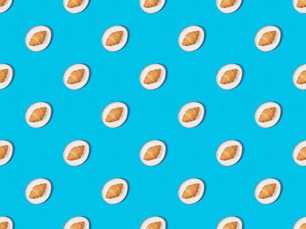 top view of fresh croissants on plates on blue, seamless background pattern