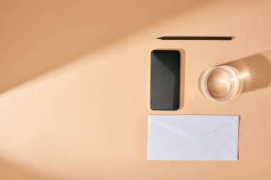 akıllı telefon, kalem, bir bardak su ve bej arka planda zarfla yatıyordu.