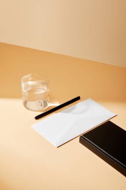 yüksek açılı zarf, kalem, bir bardak su ve bej yüzey üzerindeki siyah defter