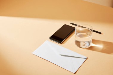 yüksek açılı akıllı telefon, zarf, bej arka planda bir bardak su ve kalem