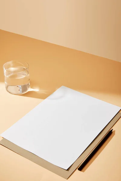 米色表面靠近水杯的纸和铅笔 — 图库照片