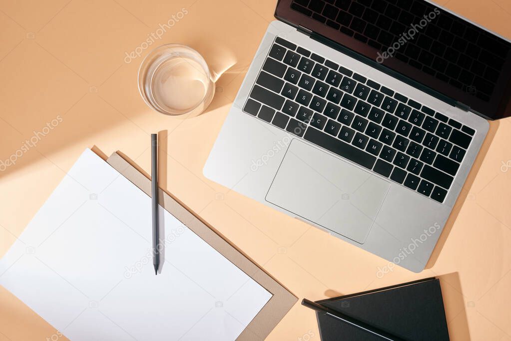 top view of sheet of paper, pencil, glass of water and notebook on beige background