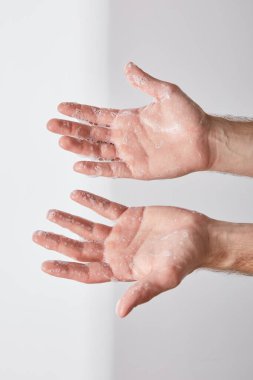 Gri arka planda sabun köpüğüyle ellerini gösteren adamın kısmi görünümü