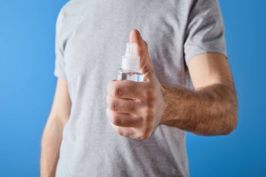 cropped view of man holding gel hand sanitizer in bottle isolated on blue clipart