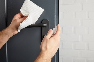 Metal kapı kolunu antiseptik ve peçeteyle dezenfekte eden adamın kısmi görüntüsü