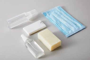 Sprey şişelerde el dezenfektanı, tıbbi maske ve gri arka planda antibakteriyel sabunla yatıyordu.