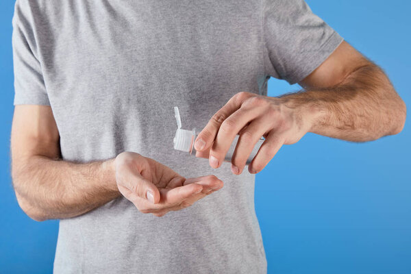 обрезанный вид человека с помощью гелевого дезинфицирующего средства для рук в бутылке, изолированной на голубом
