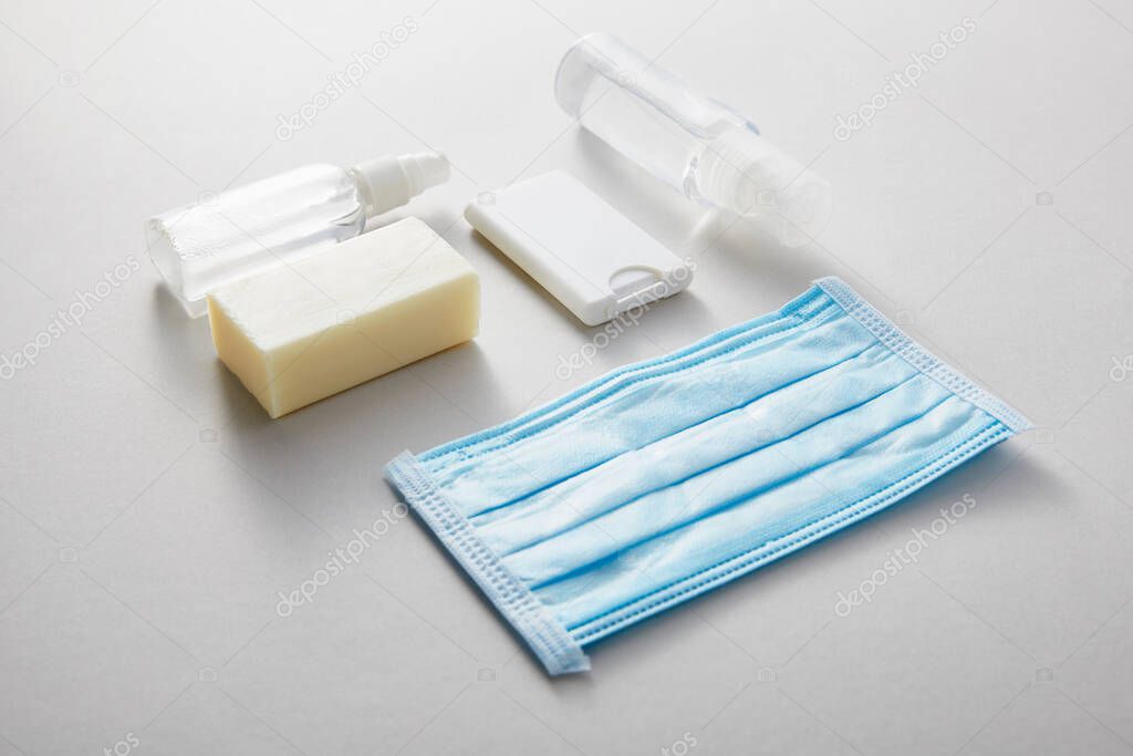 flat lay with hand sanitizer in spray bottles,  medical mask and antibacterial soap on grey background