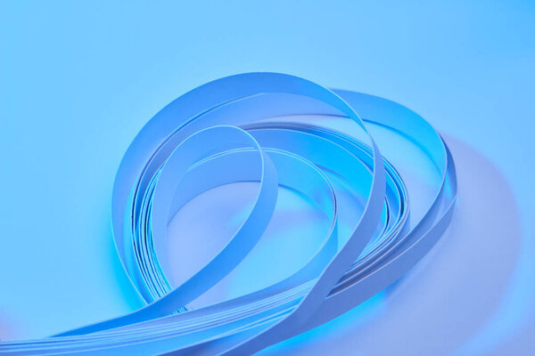 close up view of curved colorful paper stripes on neon blue background