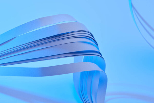 close up view of curved colorful paper stripes on neon blue background