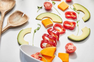 Beyaz arka planda yüksek açılı spatula, kase, kesilmiş sebzeler, mikroyeşiller ve avokado dilimleri.