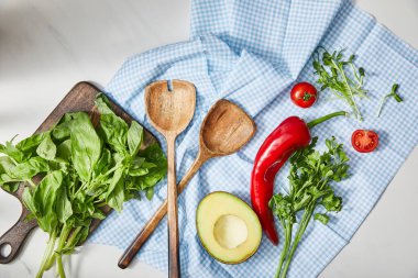 Spatulaların, maydanozların, mikro yeşilliklerin, sebzelerin ve avokadonun yarısı ekoseli kumaşın yanında fesleğenin yanında. 