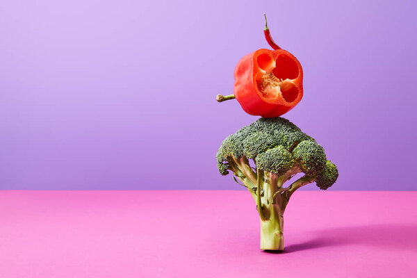 chili pepper and half of bell pepper on broccoli on purple and pink  