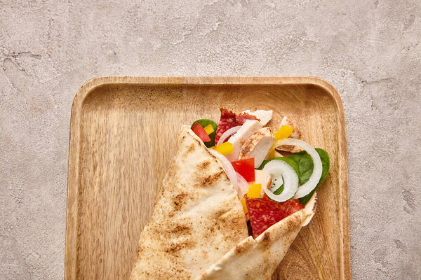 top view of fresh burrito with chicken and vegetables on board on concrete grey background