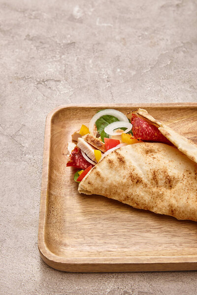 fresh burrito with chicken and vegetables on board on concrete grey background