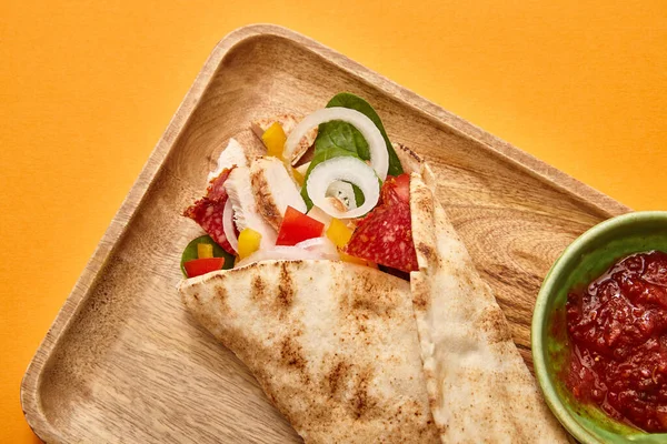 在橙红色背景的辣椒酱附近 可以看到上有鸡肉和蔬菜的新鲜墨西哥卷饼 — 图库照片