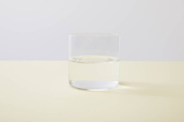 Glass with water on yellow surface isolated on grey clipart